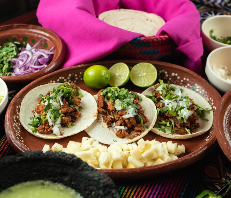 A plate of tasty meat tortillas next to raw potato cubes and lime slices